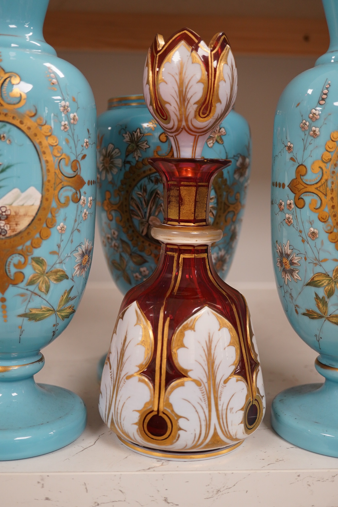 An enamelled glass garniture decorated with Egyptian scenes and a cranberry decanter, largest 29cm high. Condition - poor to fair